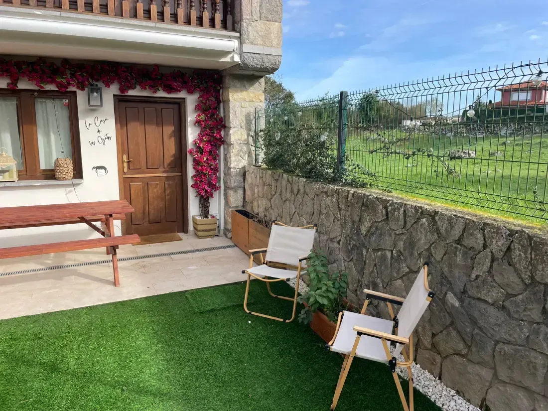 Exterior de una casa con un pequeño patio, césped verde, pared de piedra, 