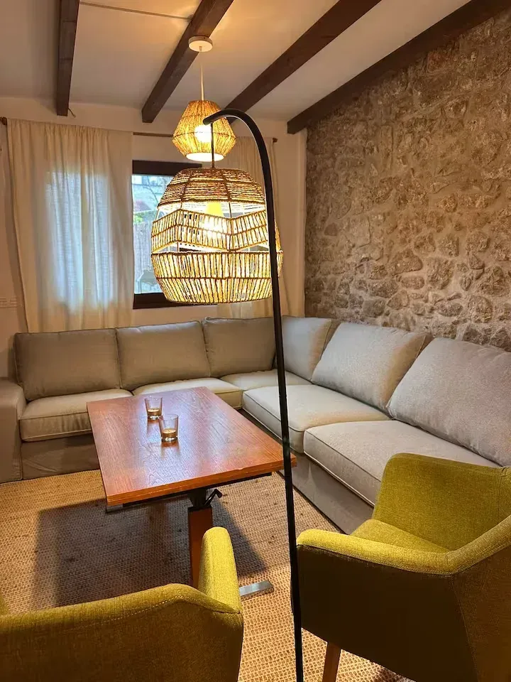 Sala de estar con sofá seccional beige, pared de piedra, vigas de madera y lámpara de mimbre.