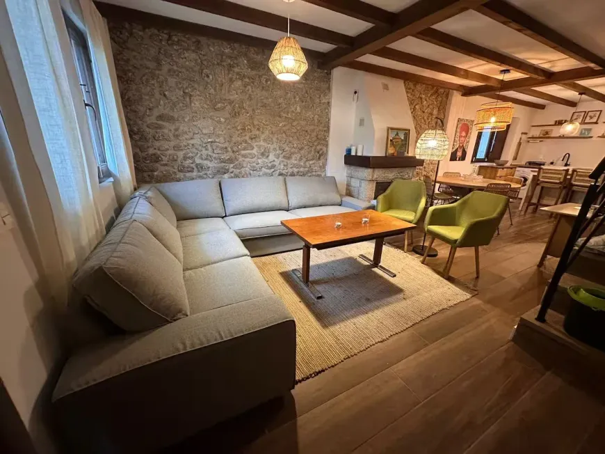 Acogedora sala de estar con pared de piedra, sofá seccional gris, vigas de madera y alfombra.