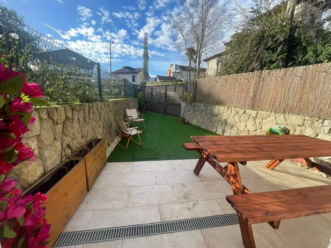 Pequeño patio trasero con mesa de picnic, césped artificial, muros de piedra y plantas con flores.