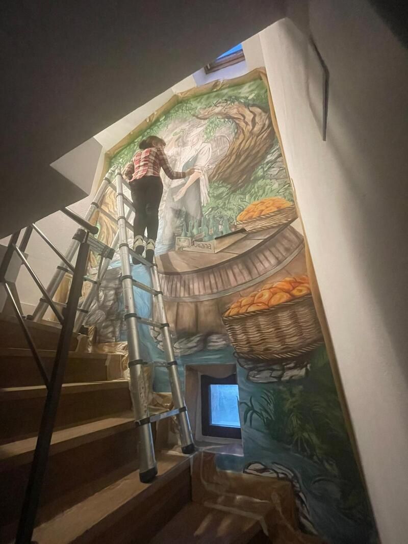 Una persona pinta un mural colorido en la pared de una escalera, con una escalera de mano y un andamio cerca