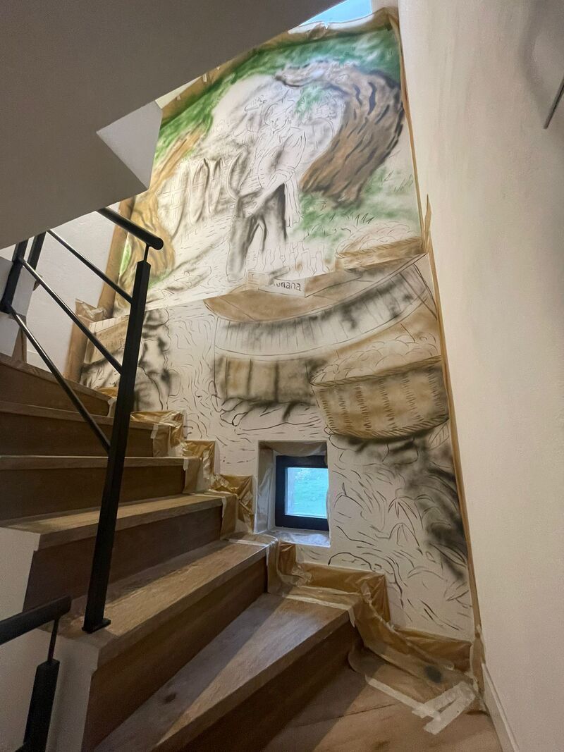Escalera con paredes de piedra, una ventana pequeña y un dibujo tipo mural sobre los escalones