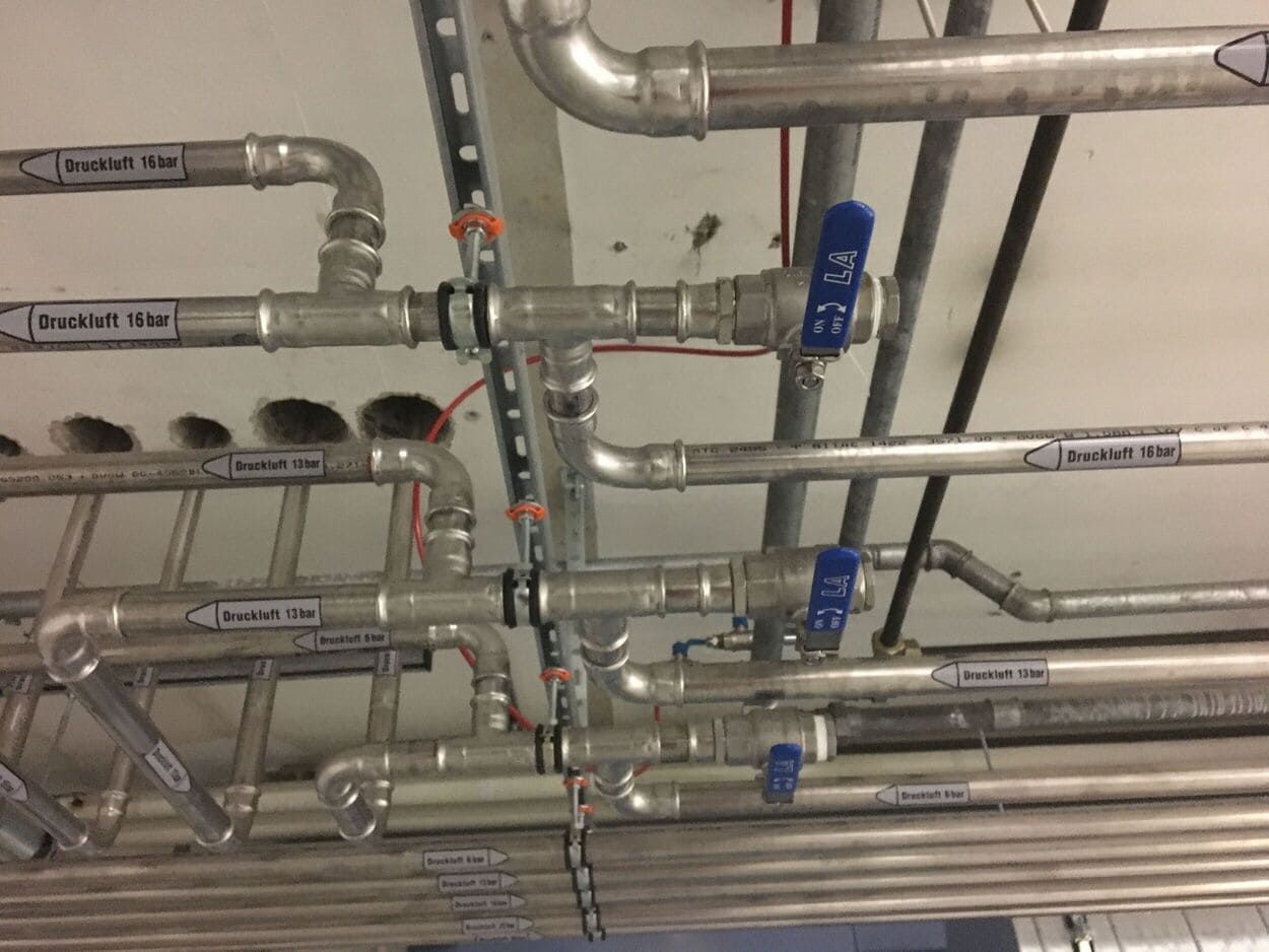 Decke mit freiliegenden Metallrohren und blau griffigen Ventilen in einem industriellen Interieur
