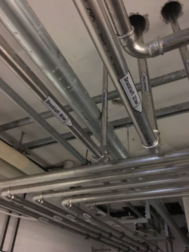 Decke mit freiliegenden silbernen Metallrohren und Leitungen in einem industriellen Versorgungsraum