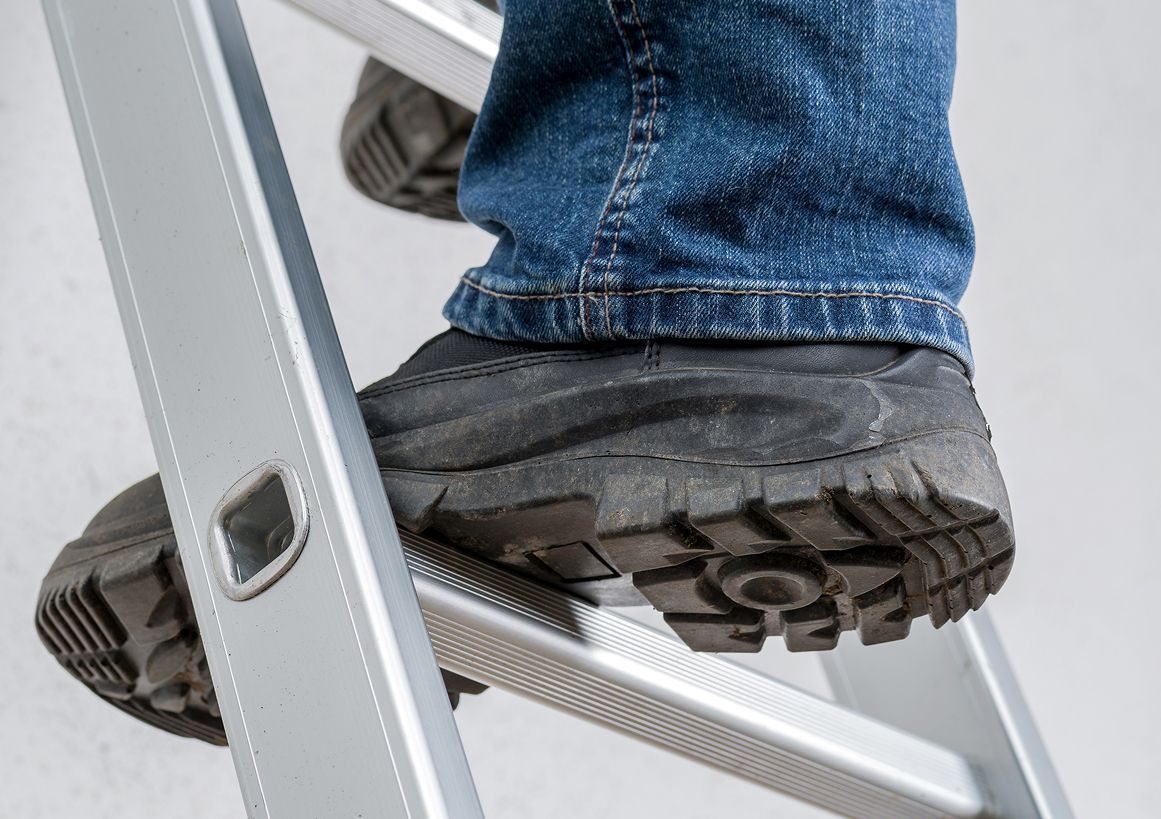 Fuß auf einer Metallleitersprosse, Jeans und schwarze Arbeitsstiefel im Freien