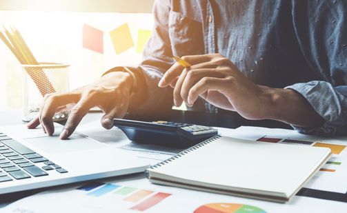 Person arbeitet mit Laptop und Handy an Dokumenten