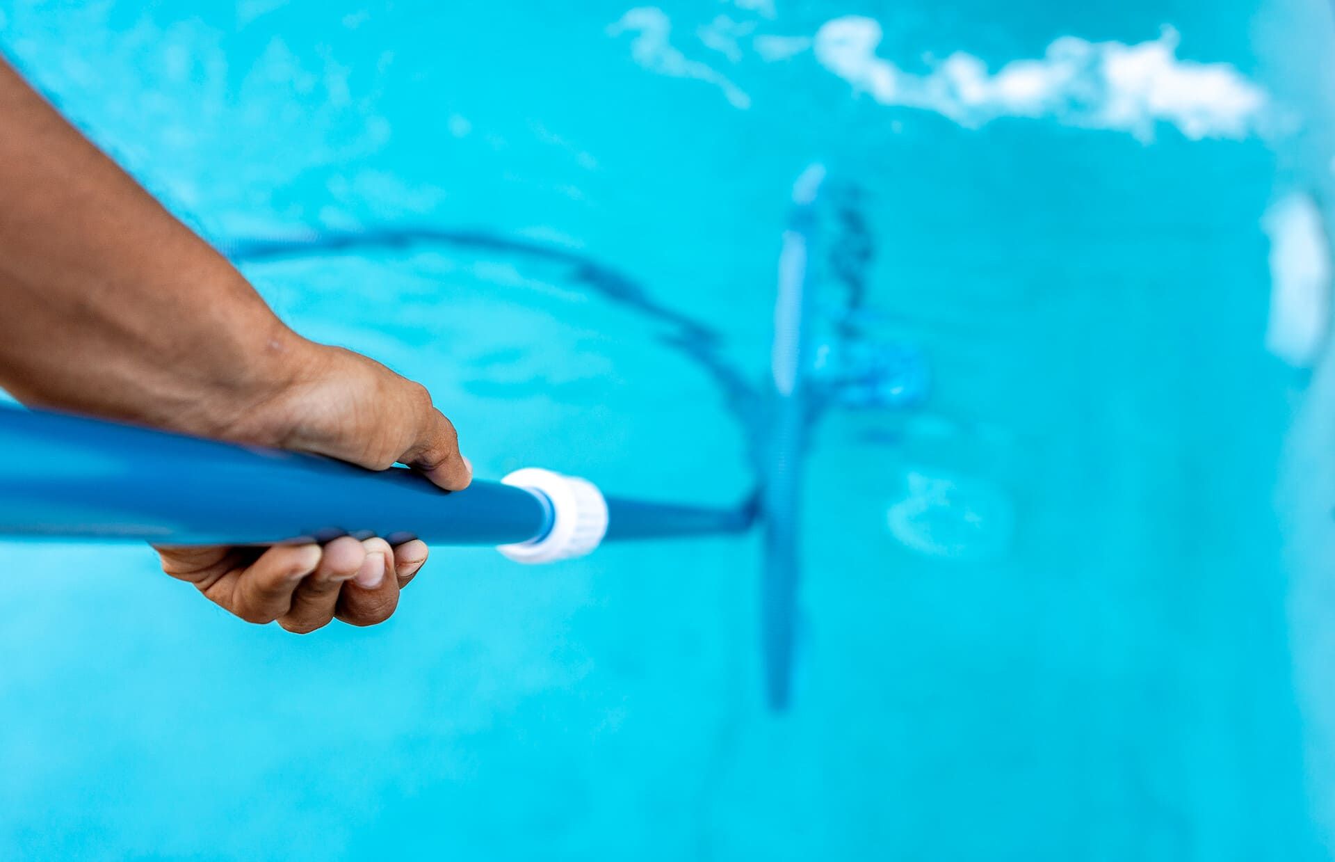 Persona que utiliza un cepillo de piscina azul para limpiar una piscina turquesa.