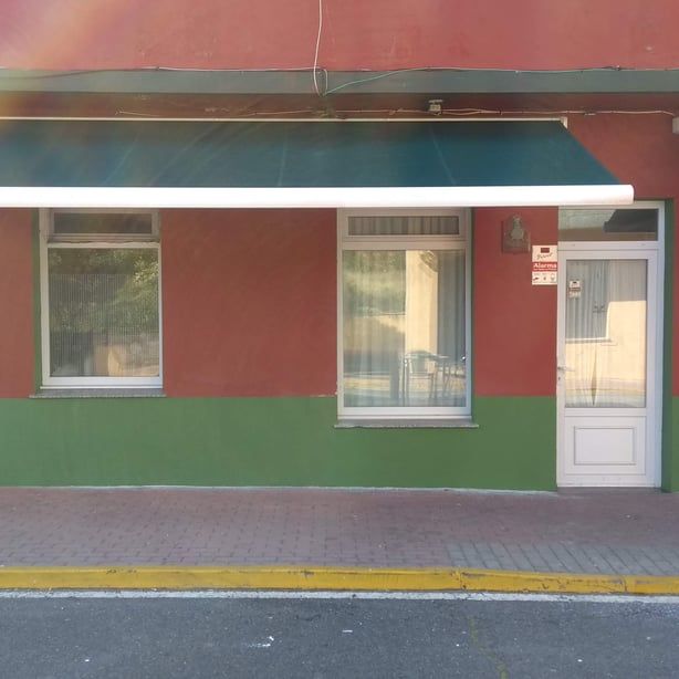 Un edificio rojo y verde con un toldo azul sobre la puerta de entrada.