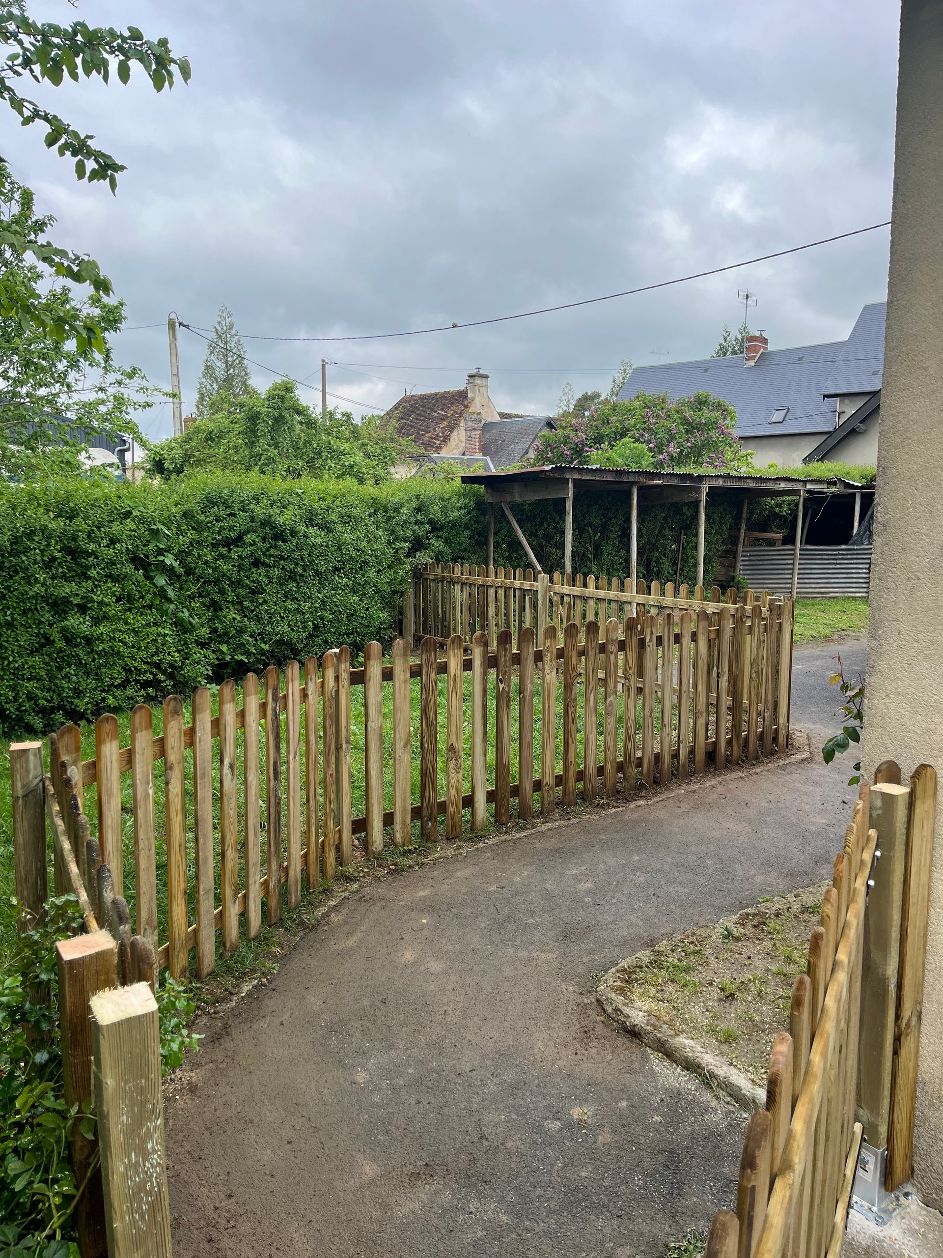 Allée en gravier sinueuse longeant une clôture en bois et une haie verte dans un jardin.