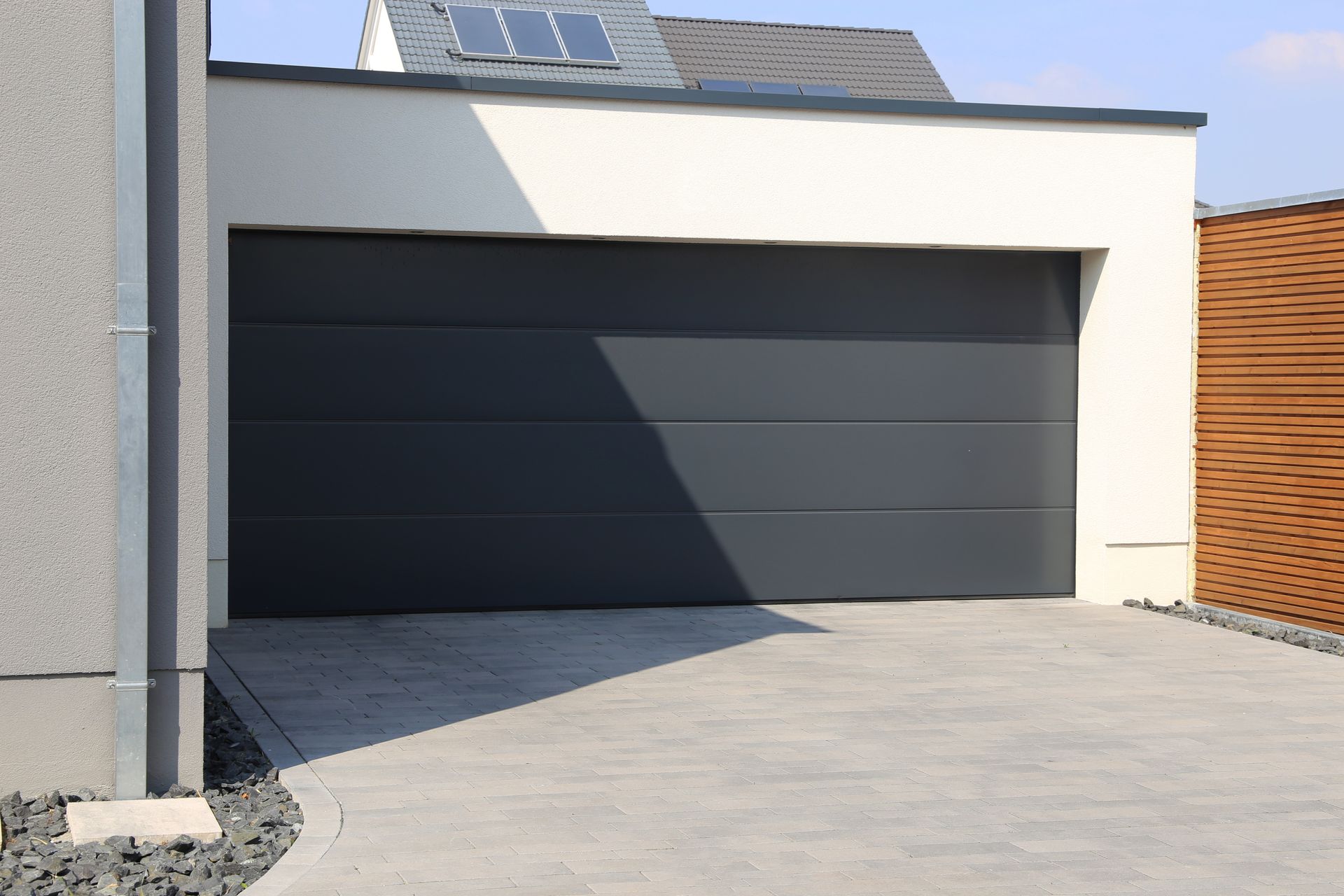 Maison moderne avec porte de garage foncée et allée gris clair baignée de soleil