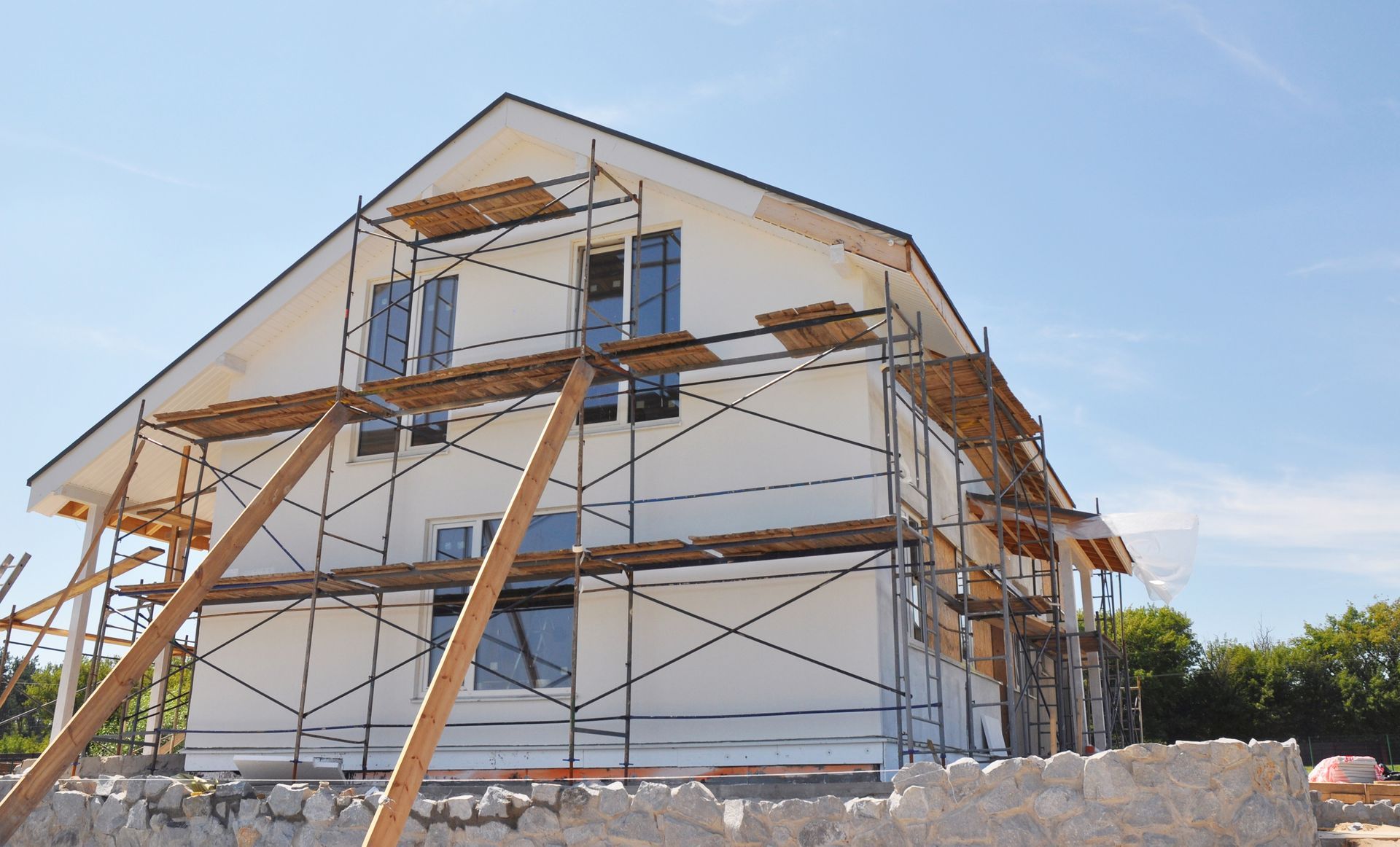 Maison en construction avec échafaudages et supports en bois sous un ciel bleu clair