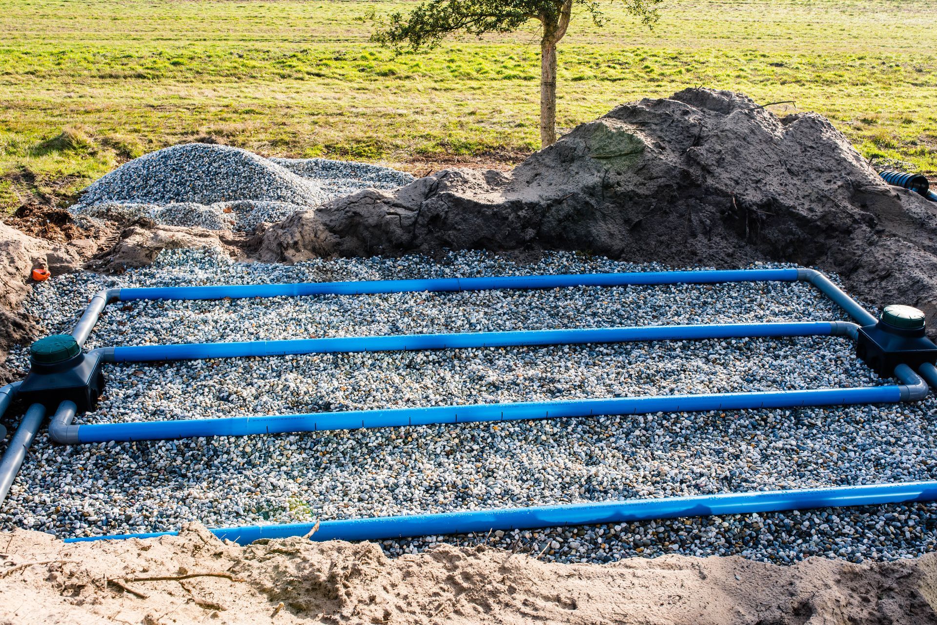 Cadre en tuyau PVC bleu posé à même la terre, à côté de tas de gravier, sur un chantier de construction.