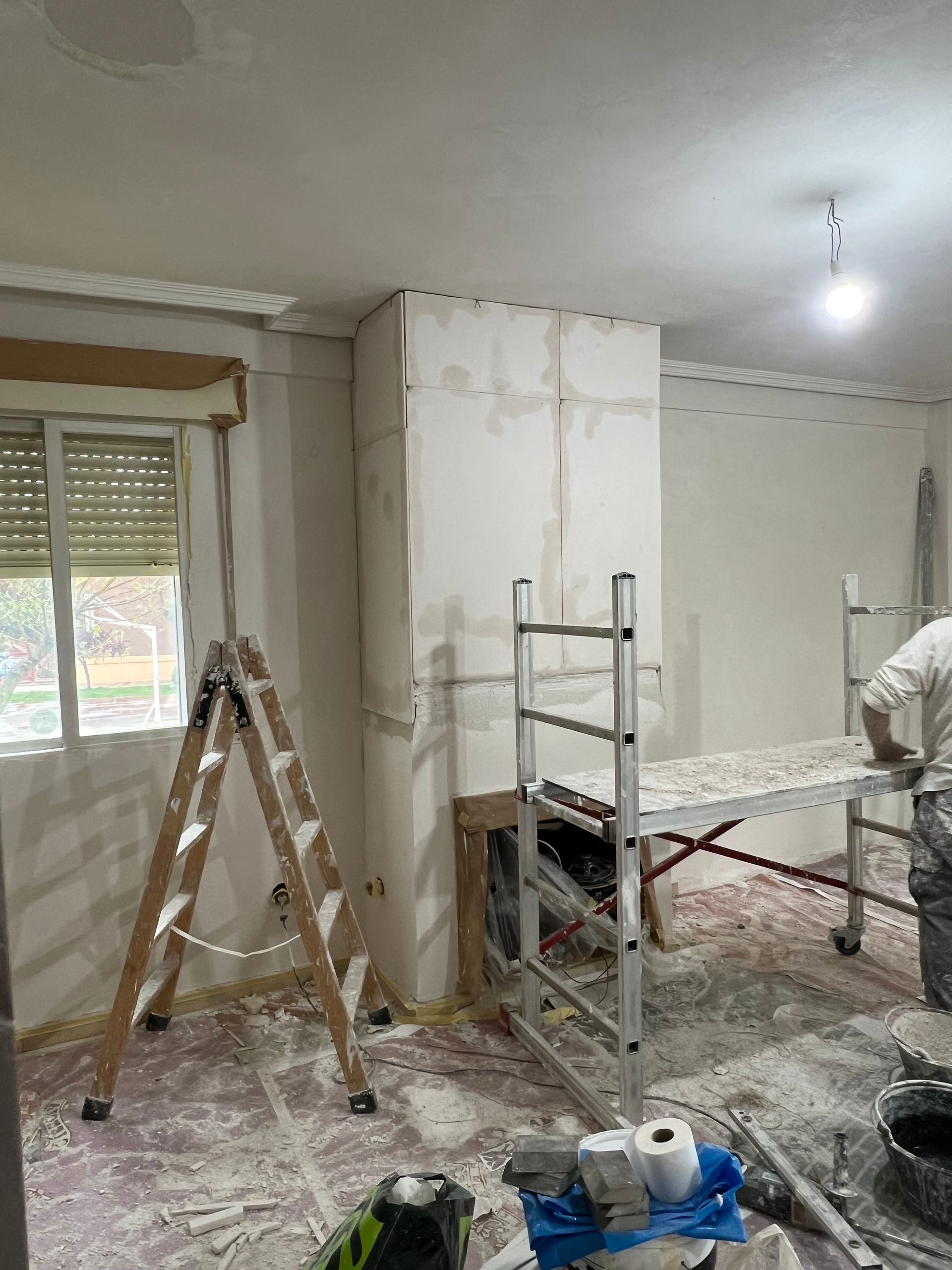 Pièce intérieure en rénovation avec échafaudage, échelle, sol poussiéreux et ouvrier peignant un mur