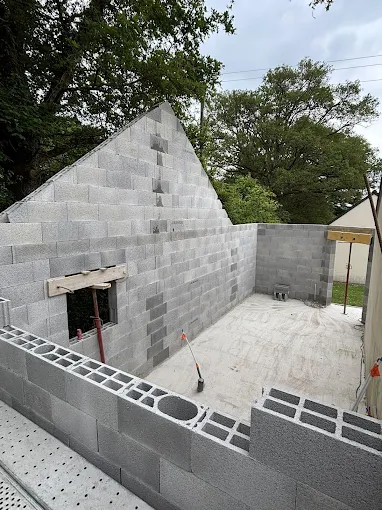 Maison en parpaings partiellement construite, avec toit en pente et cour ouverte, en construction