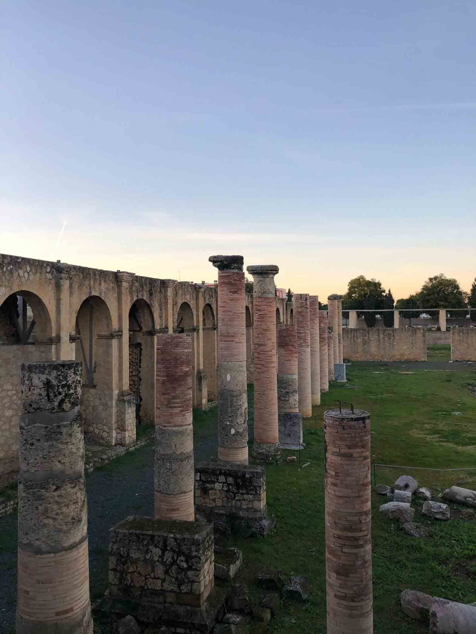 Ruinas de un antiguo anfiteatro, probablemente romano, con gradas de piedra y tramos de muralla. Exterior diurno.