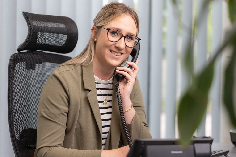 Frau mit Brille lächelt, während sie in einem Büro am Tischtelefon telefoniert.