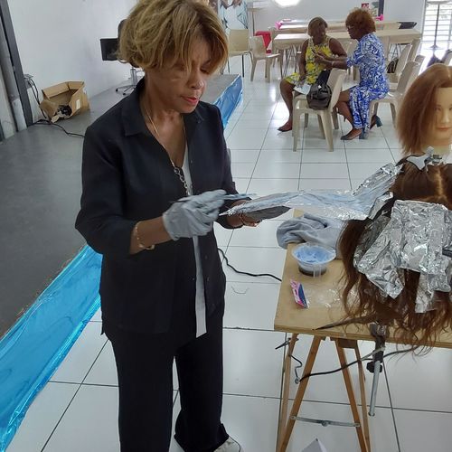 Une coiffeuse en train d'appliquer un décolorant sur une perruque