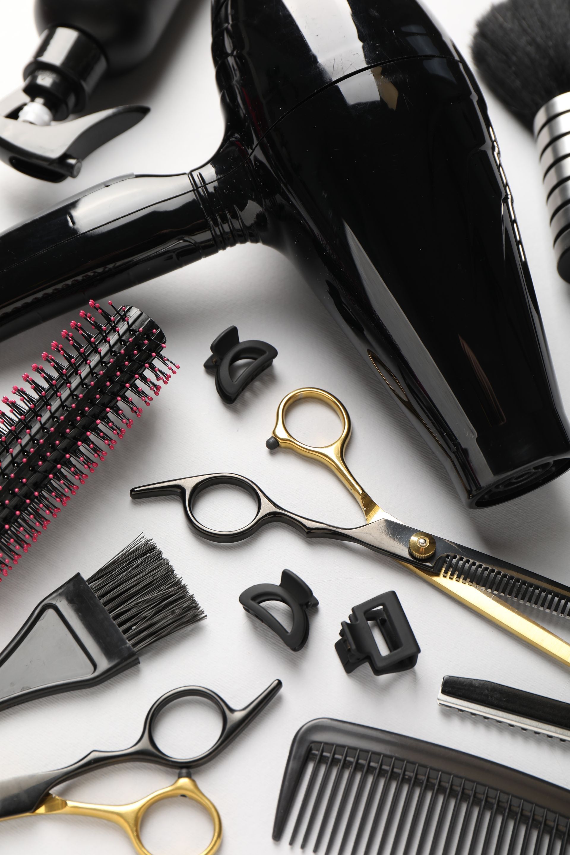 Assortiment d'outils et de peignes noirs pour la coiffure sur fond blanc, comprenant des ciseaux et des brosses à cheveux.