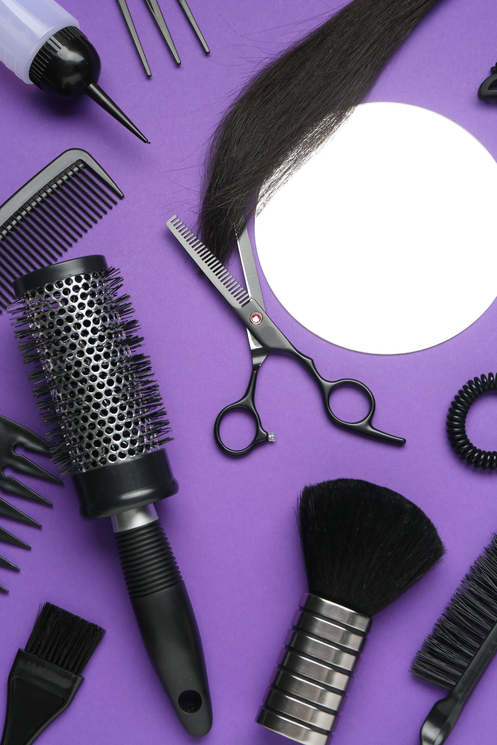 Outils de coiffure sur fond violet : peignes, ciseaux, brosses et miroir rond