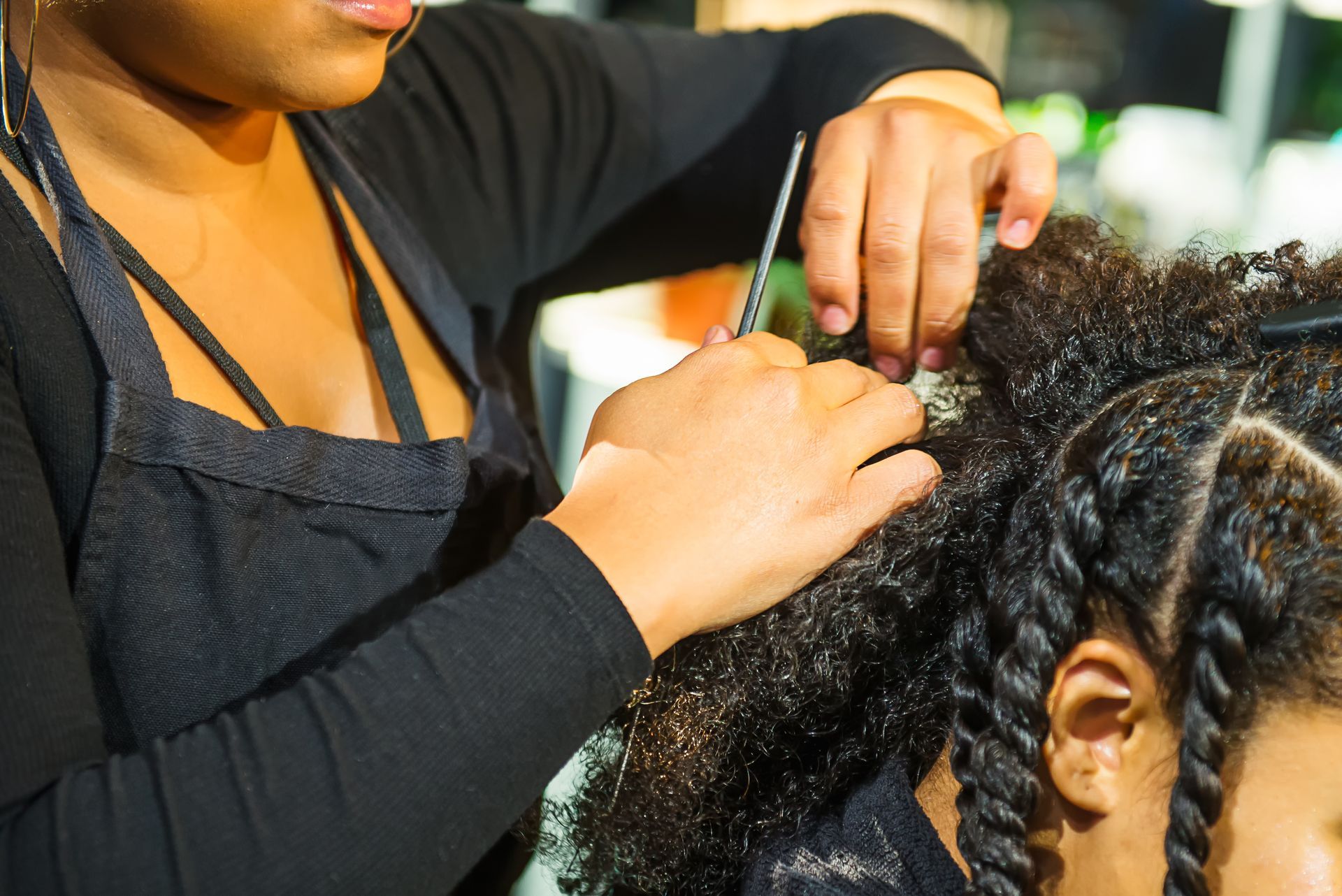 Une coiffeuse tresse les cheveux d'une cliente dans un salon, gros plan sur ses mains et le peigne.