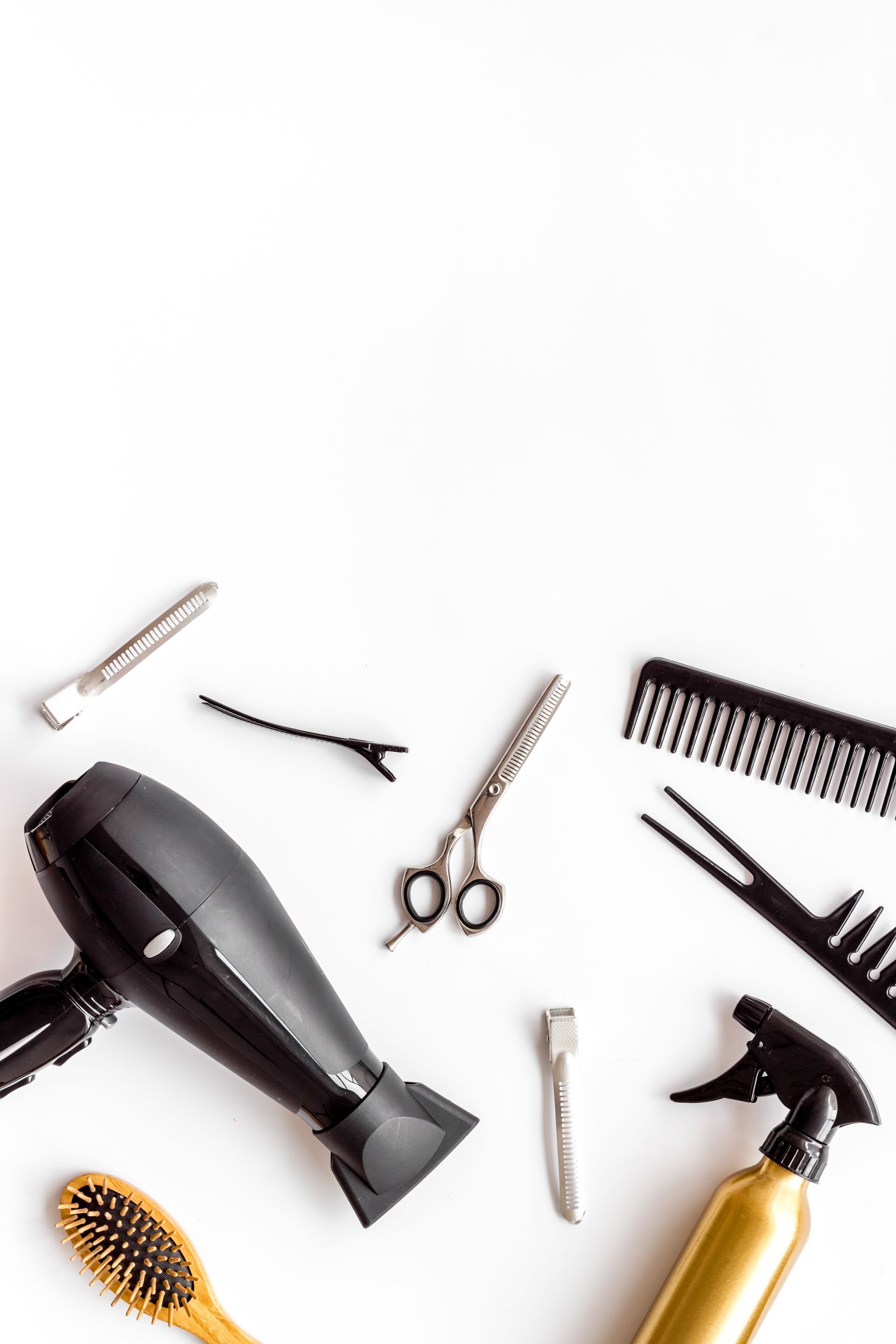Accessoires de coiffure variés sur fond blanc, comprenant sèche-cheveux, brosse, peigne, ciseaux, pinces et vaporisateur.