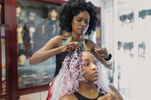 Une coiffeuse coiffe les cheveux bouclés d'une cliente dans un salon, tandis que celle-ci est assise.