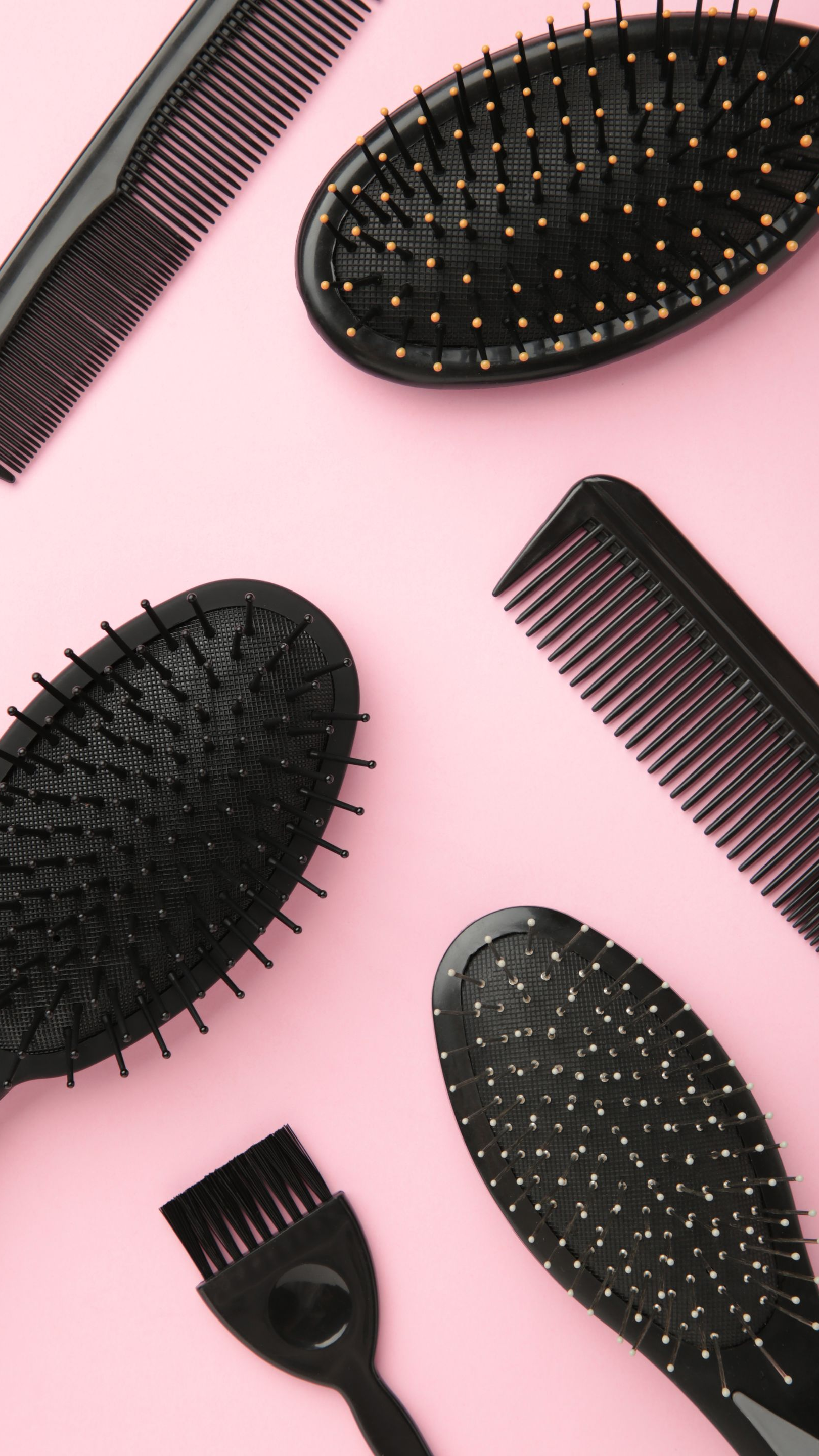 Assortiment de brosses et de peignes à cheveux noirs disposés sur un fond rose.