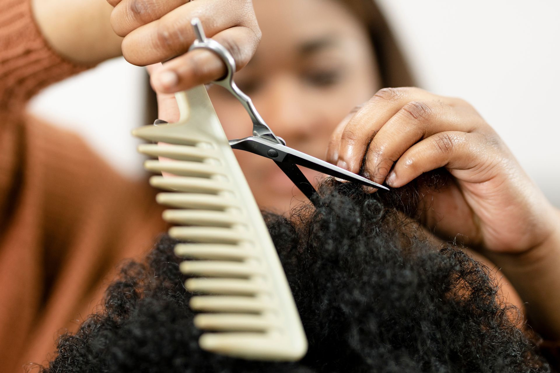 Coiffeuse coupant des cheveux bouclés avec des ciseaux et un peigne en gros plan