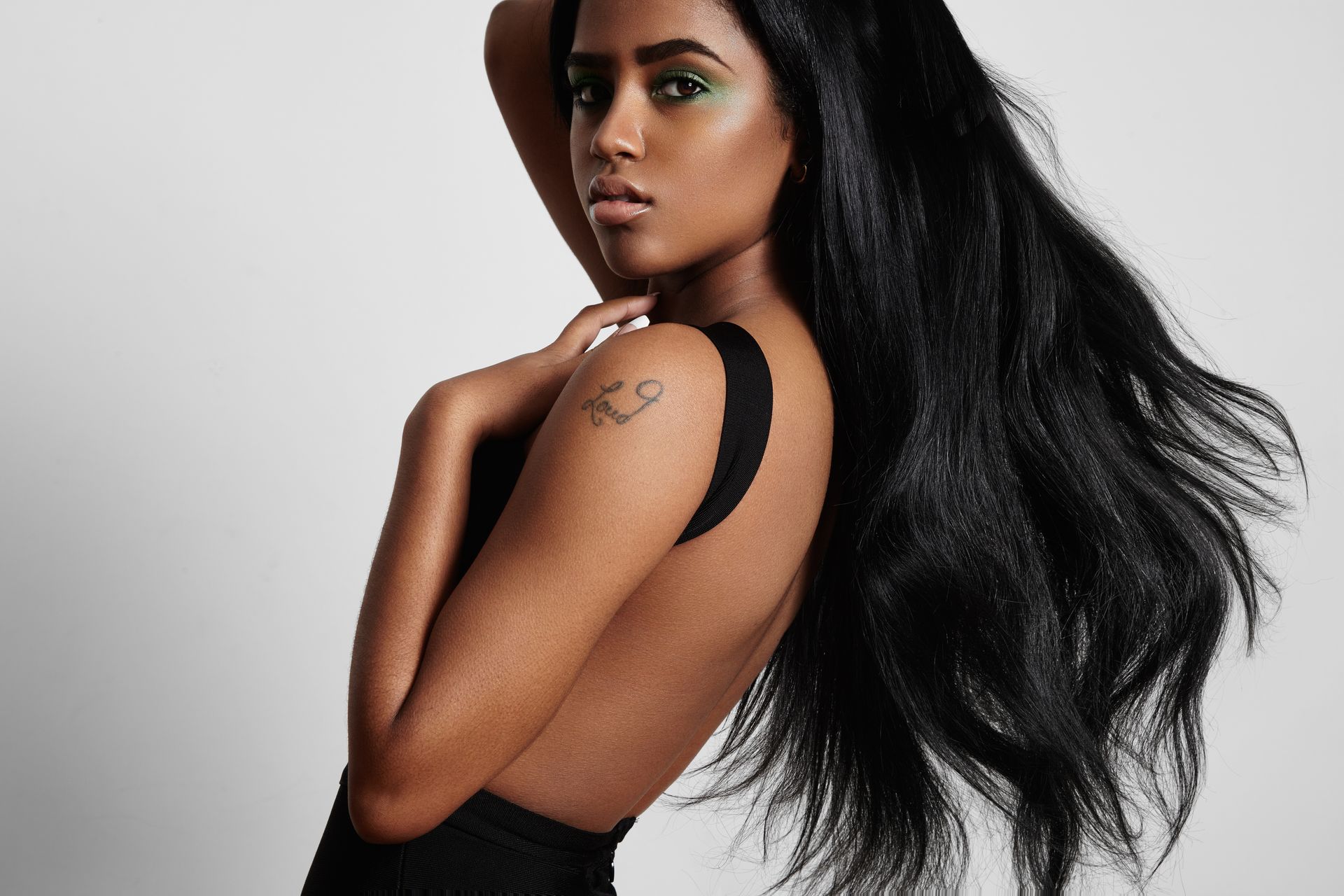 Femme aux longs cheveux noirs posant en haut noir sur fond gris clair