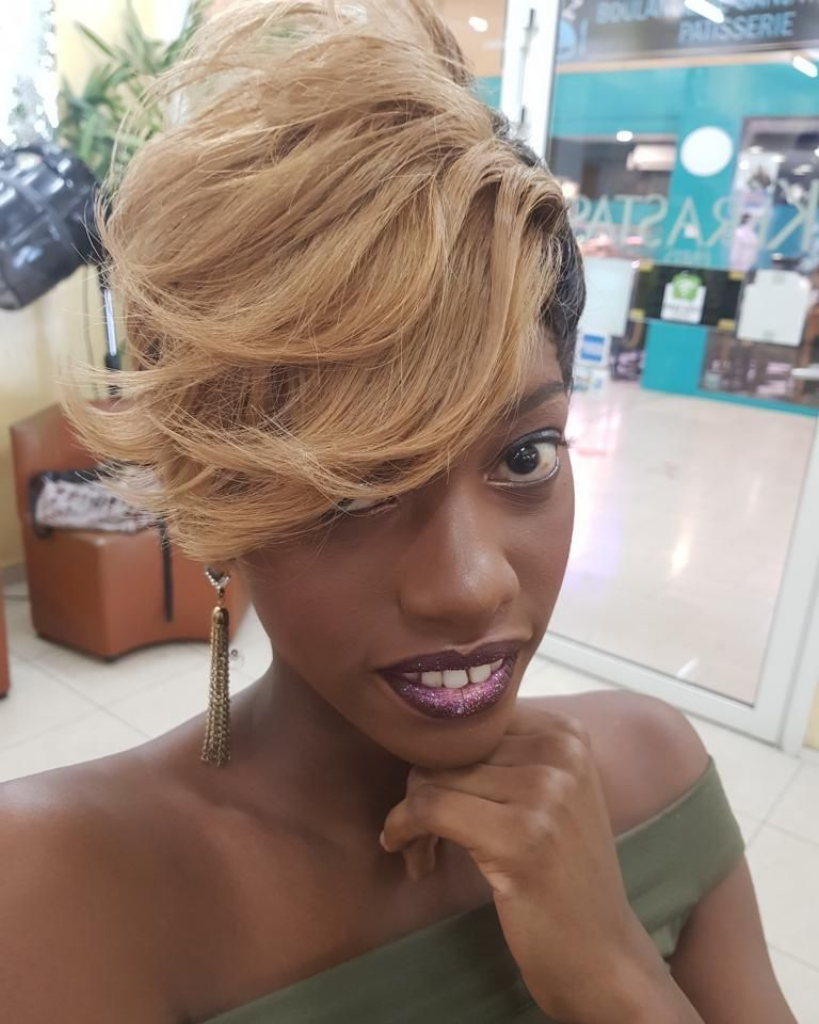 Selfie en gros plan d'une femme aux cheveux blonds courts et au rouge à lèvres violet dans un magasin.