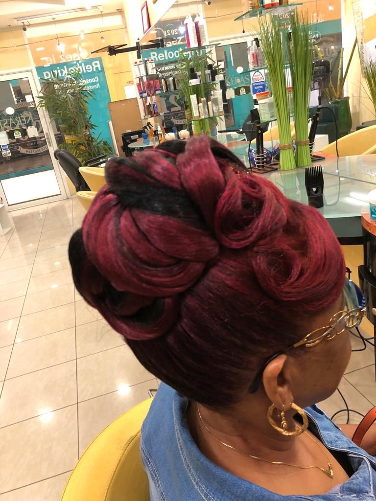 Femme avec une coiffure tressée bordeaux et des lunettes assise dans un salon de coiffure d'un centre commercial
