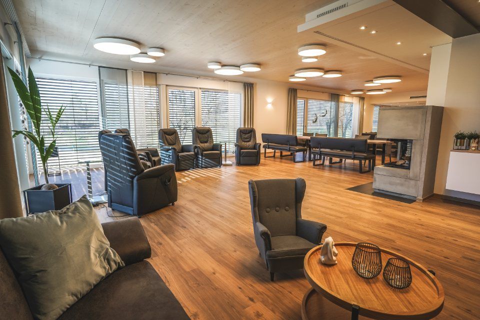 Die Hände einer Person ruhen auf den Schultern einer älteren Person; beide scheinen sich im Inneren eines Raumes zu befinden.