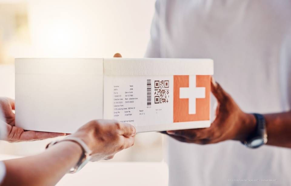 Eine Person übergibt einer anderen Person eine weiße Schachtel mit einem orangefarbenen Kreuz.