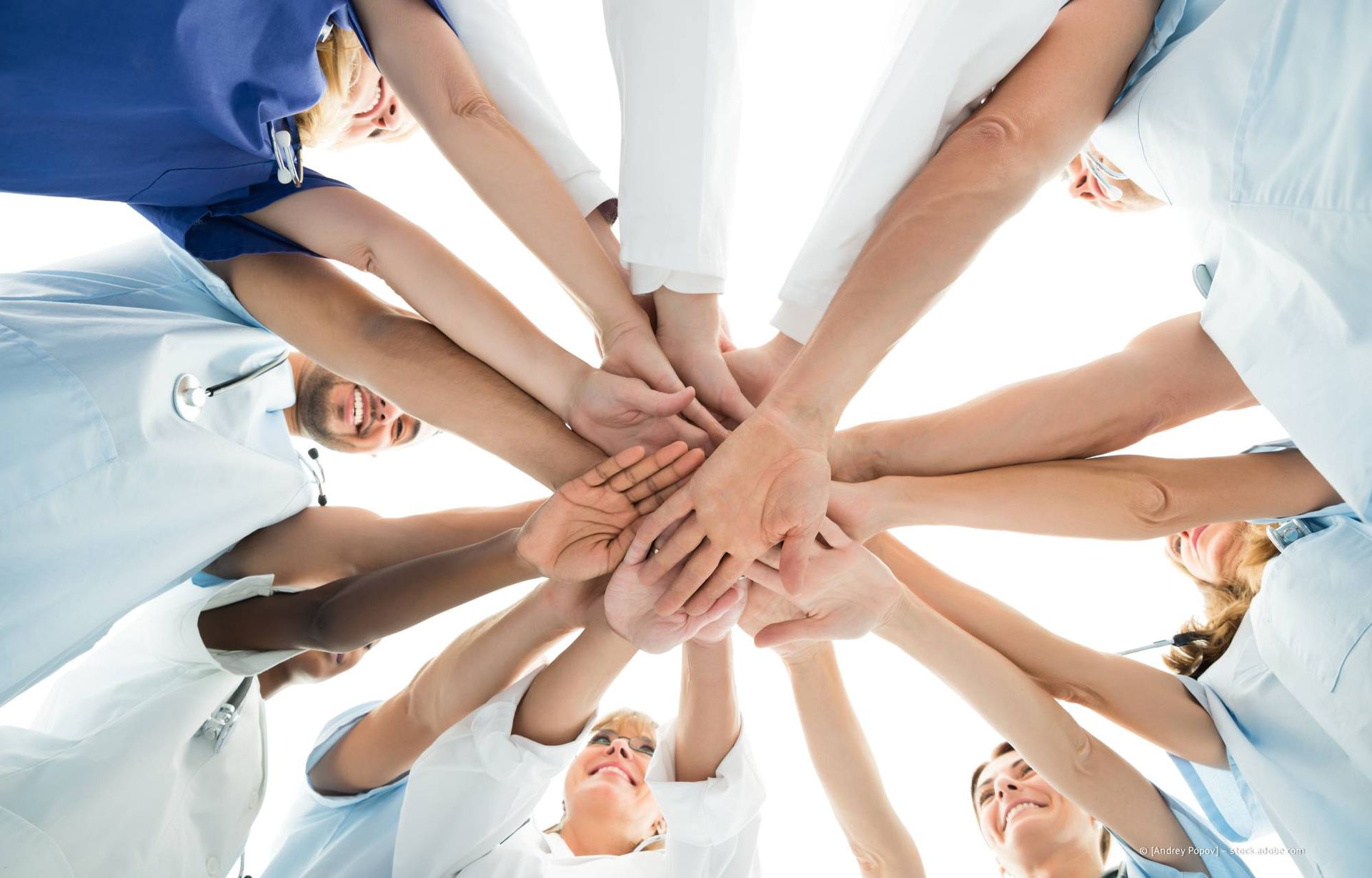 Medizinisches Fachpersonal in OP-Kleidung und Laborkitteln, die Hände im Kreis zusammengelegt – Teamwork.