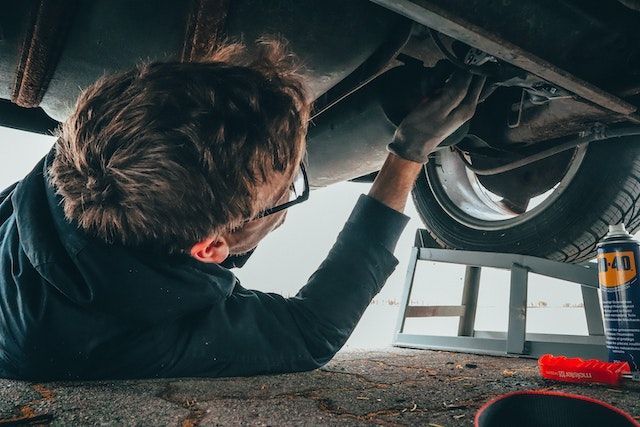 Un hombre está tendido en el suelo trabajando en un coche.