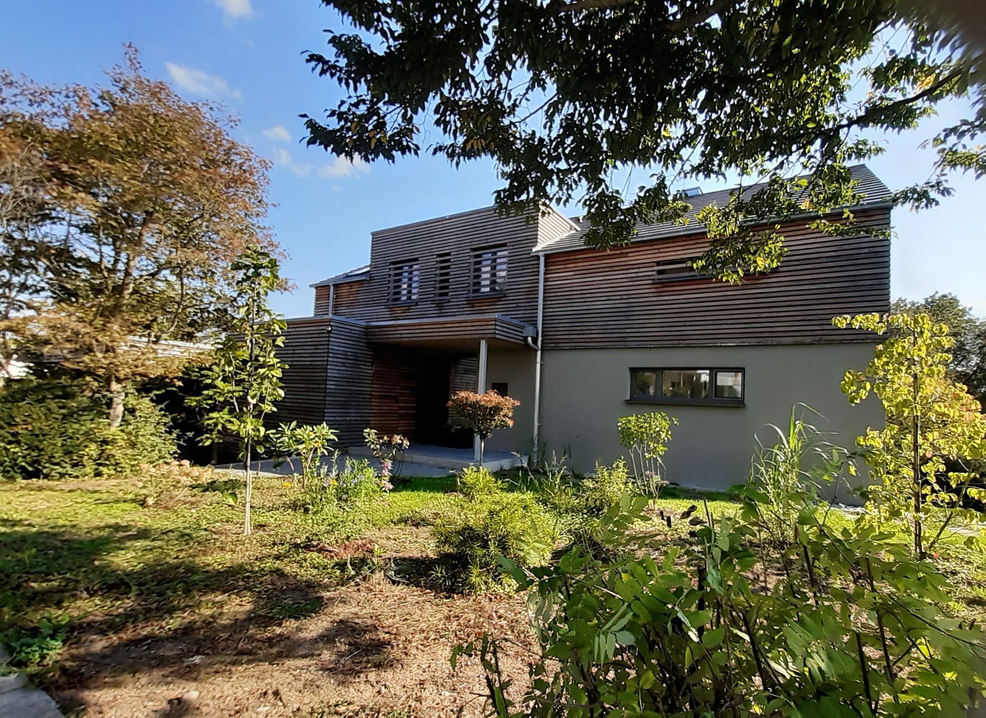 An einem sonnigen Tag ist ein großes Haus von Bäumen und Gras umgeben.