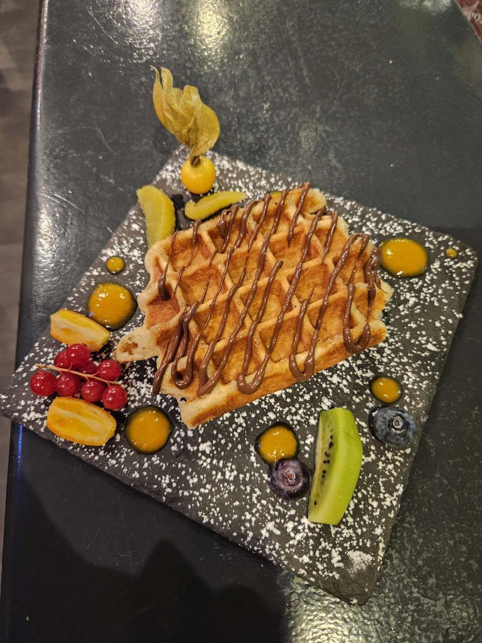 Une gaufre sur une assiette avec des fruits et du sucre glace