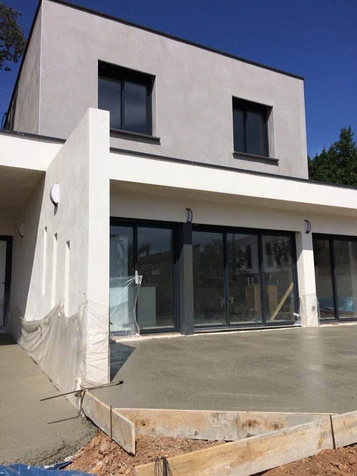 Maison moderne à deux étages avec terrasse en béton fraîchement coulé. Murs gris, fenêtres à cadre noir et portes coulissantes en verre.