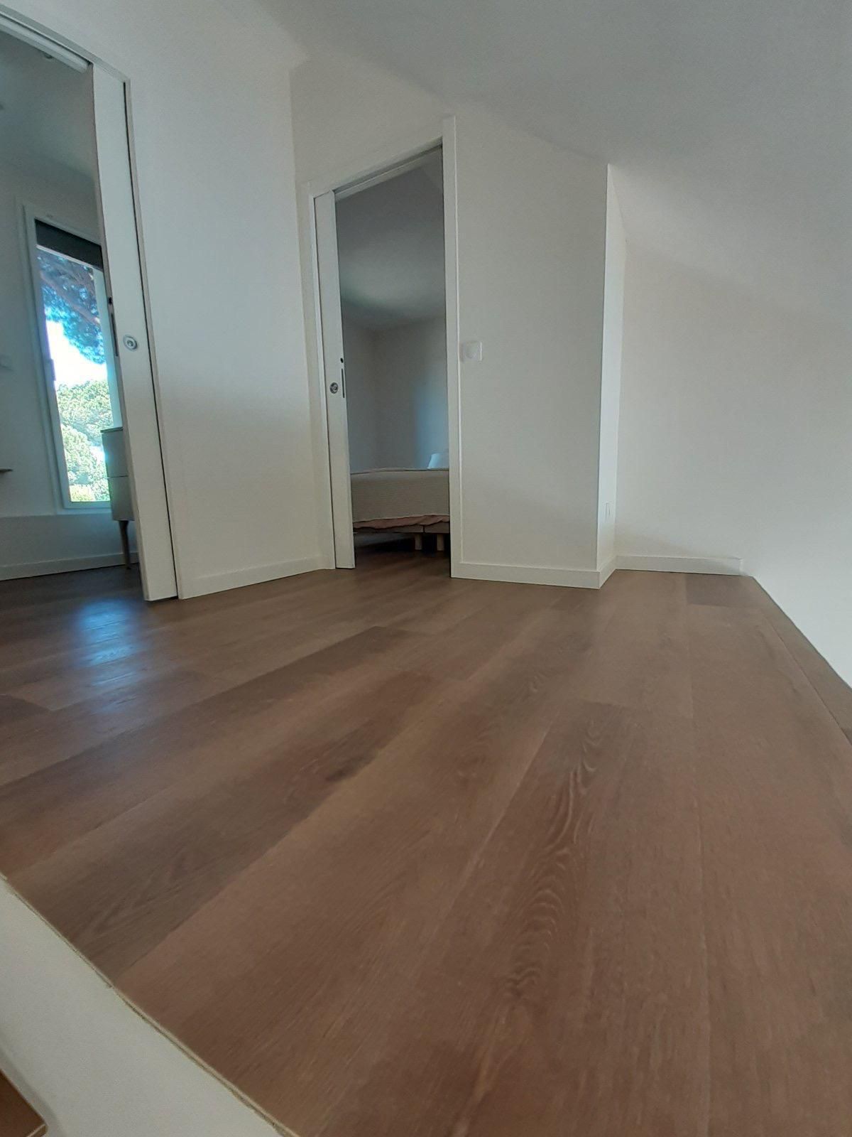 Couloir avec sol en bois, portes et murs blancs.