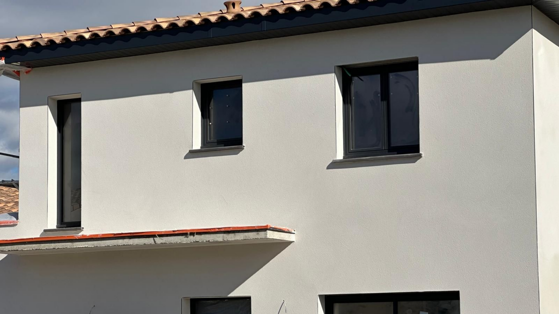 Bâtiment blanc de deux étages avec des encadrements de fenêtres foncés et un toit de tuiles rouges.