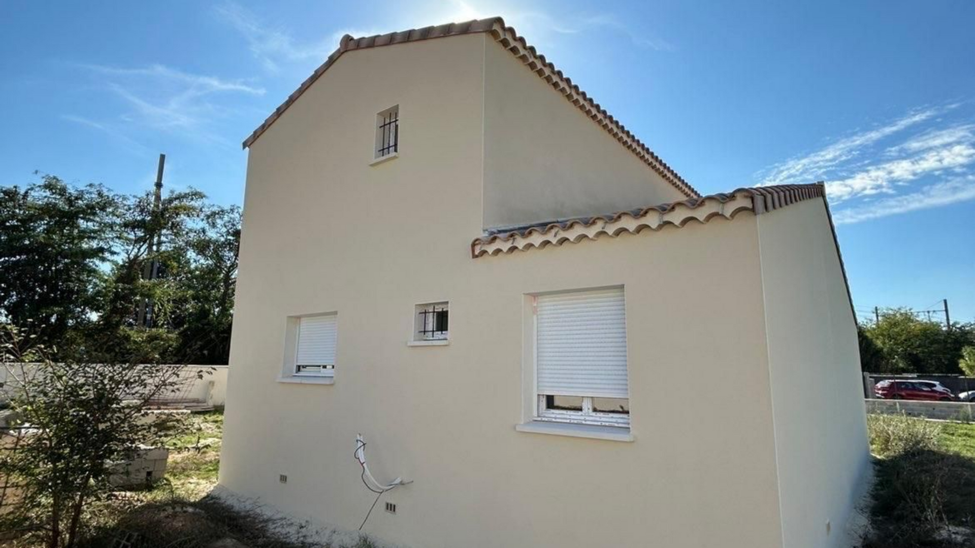 Maison beige au toit de tuiles sous un ciel d'un bleu éclatant.