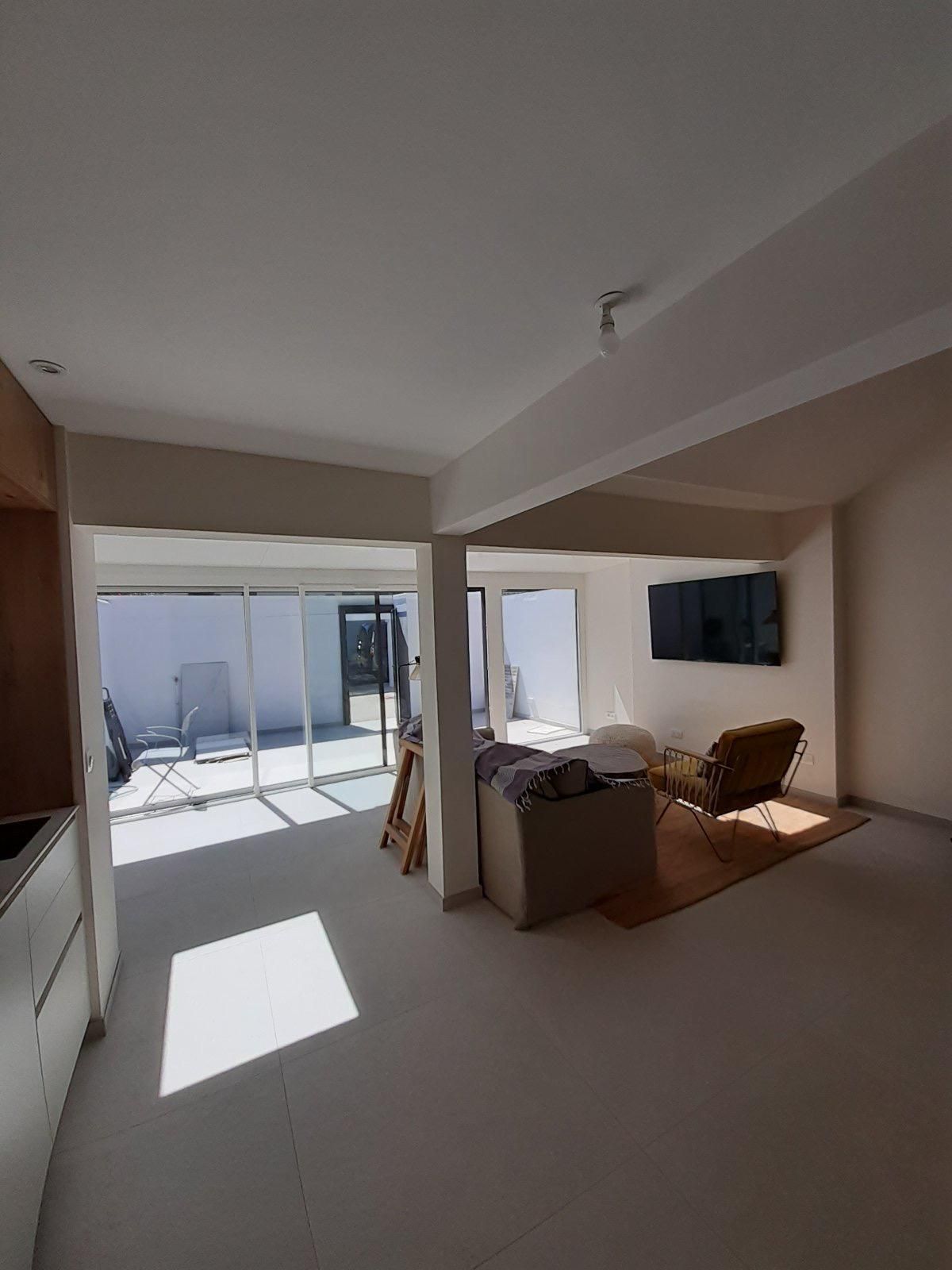 Salon lumineux avec portes-fenêtres donnant sur une terrasse. Télévision, meubles et lumière naturelle abondante.