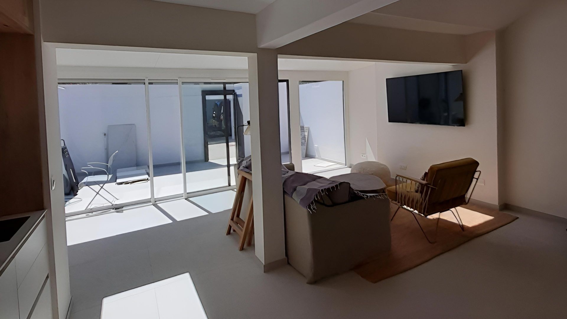 Salon avec vue sur terrasse ; canapé, fauteuil, télévision et porte ouverte. Murs blancs, lumineux et modernes.