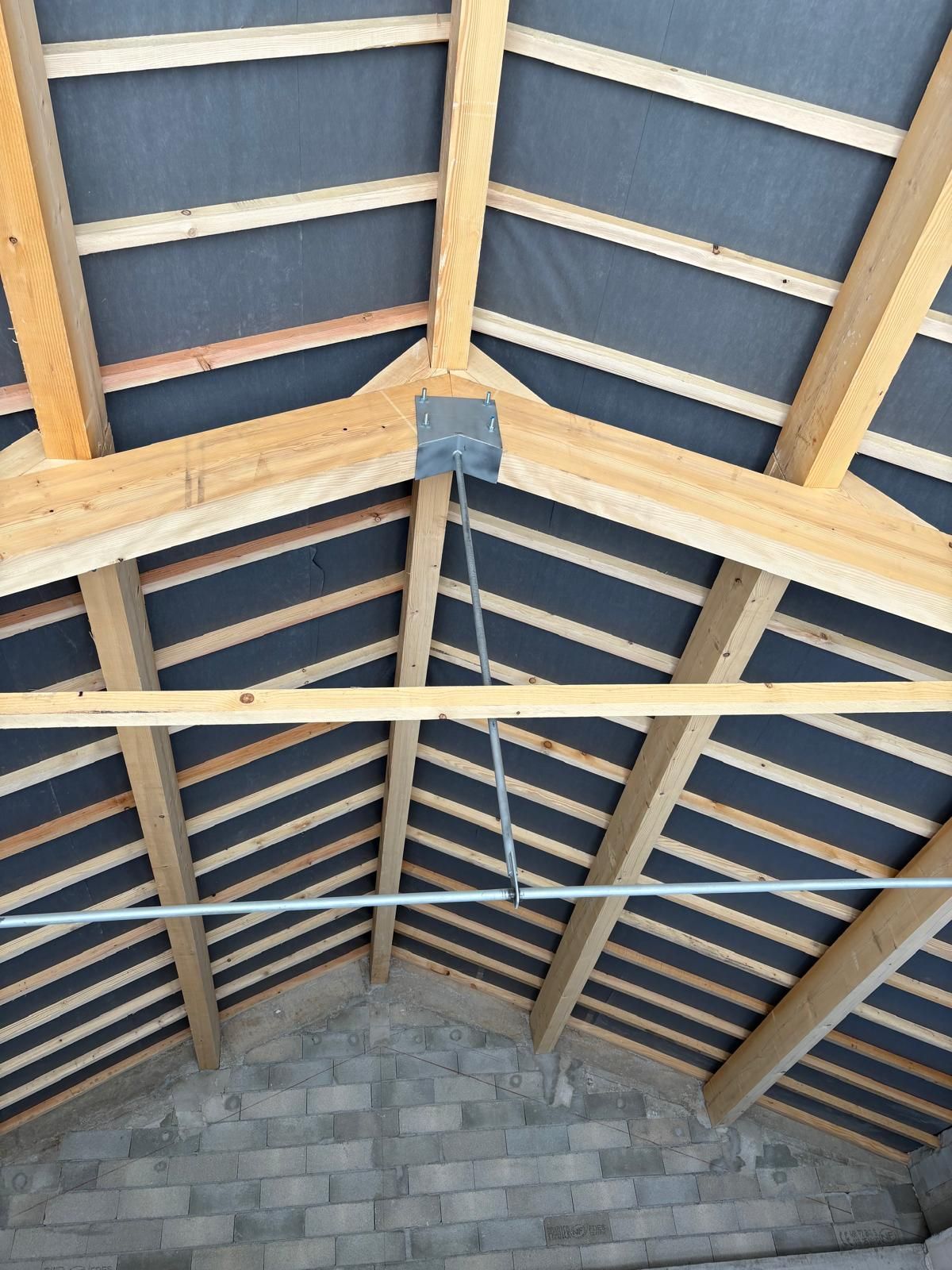 Vue intérieure d'une charpente de toit en bois avec chevrons et luminaire suspendu, adossée à un mur en parpaings.