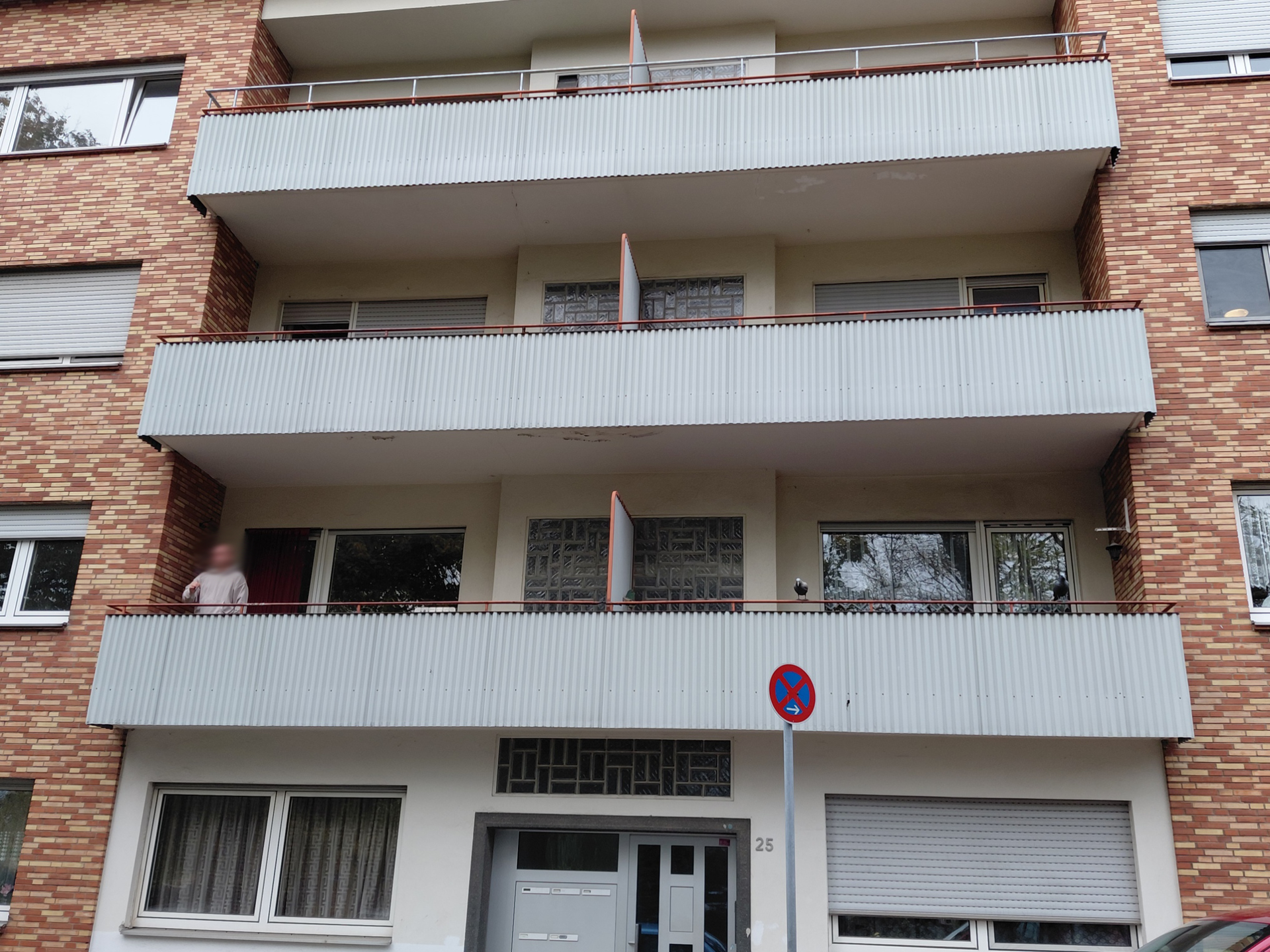 Backstein-Mehrfamilienhaus mit weißen Balkonen und einem Parkverbotsschild über dem Eingang