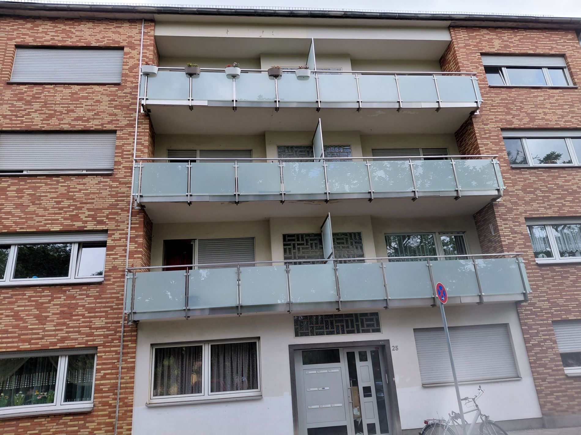 Mehrfamilienhaus aus Backstein mit Balkongeländern aus Glas und geschlossenen Fensterläden