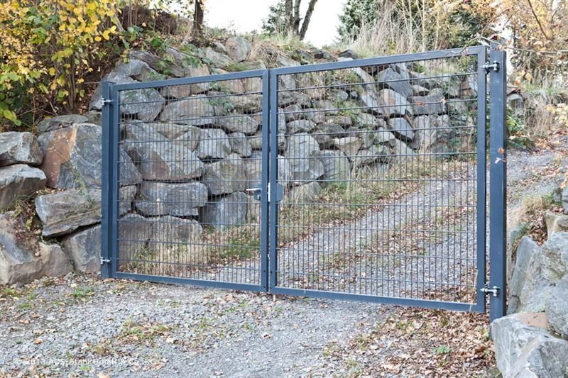Vor einer Steinmauer steht ein Metalltor.