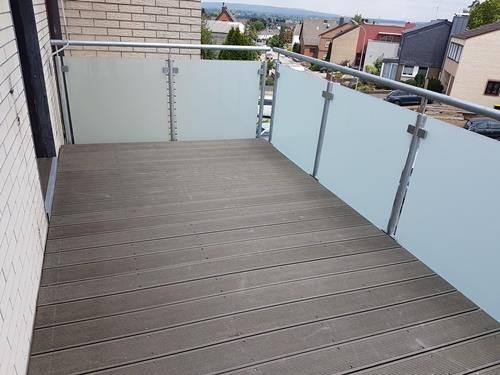 Ein Balkon mit Holzdeck und Glasgeländer.