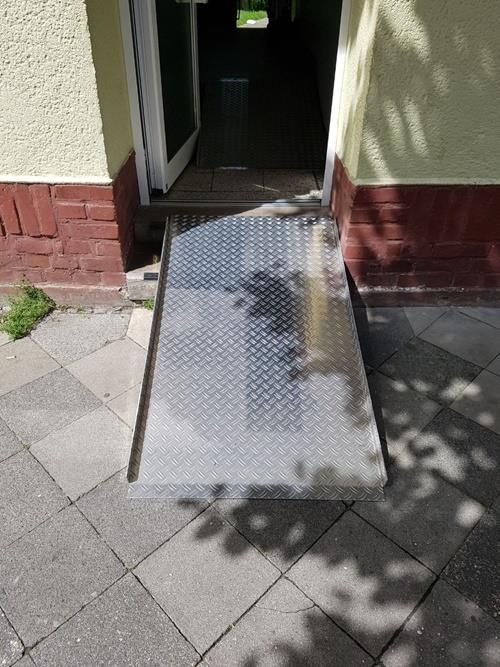 Auf dem Bürgersteig vor einem Gebäude steht eine Metallrampe.