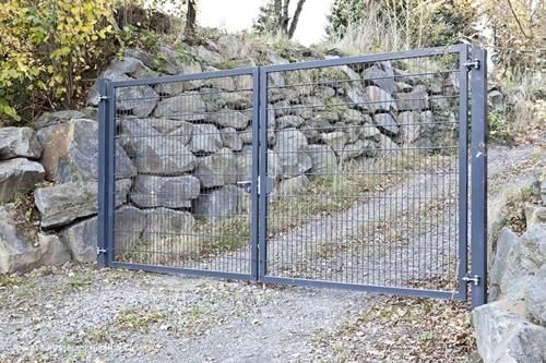 Vor einer Steinmauer steht ein Metalltor.